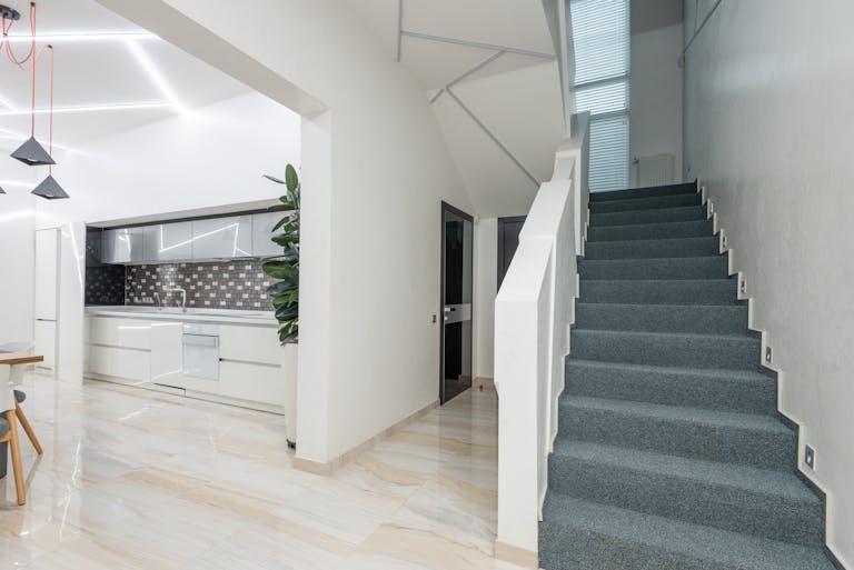 Stairway in corridor of spacious house near light kitchen with minimalist furniture and modern appliances